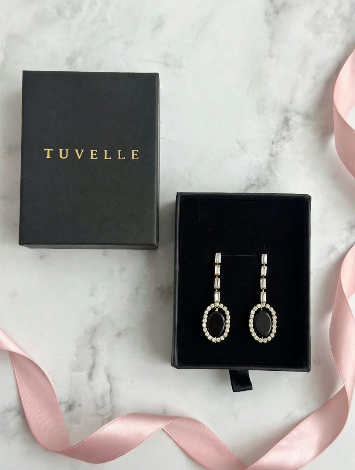 Noor black oval halo drop earrings hanging beneath a pink ribbon