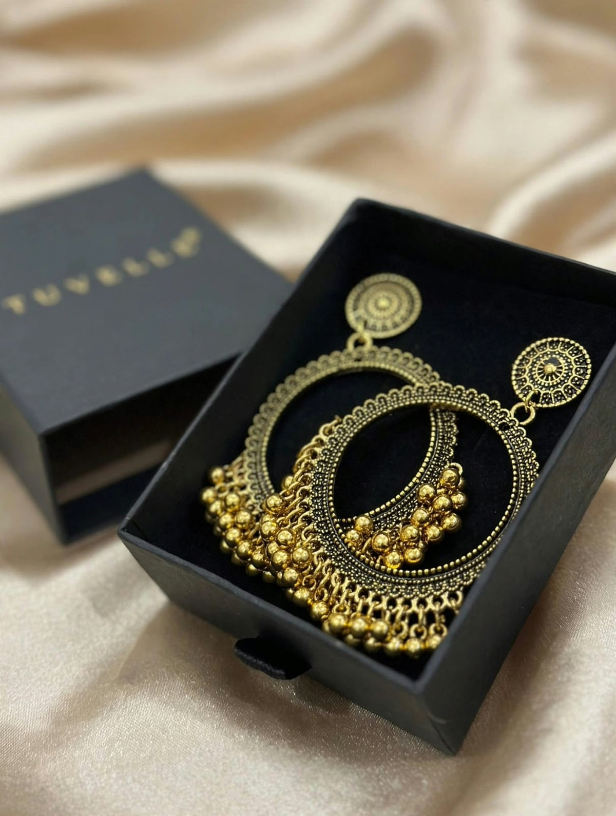 Angled view of gold-tone chandbali earrings in a black jewellery box