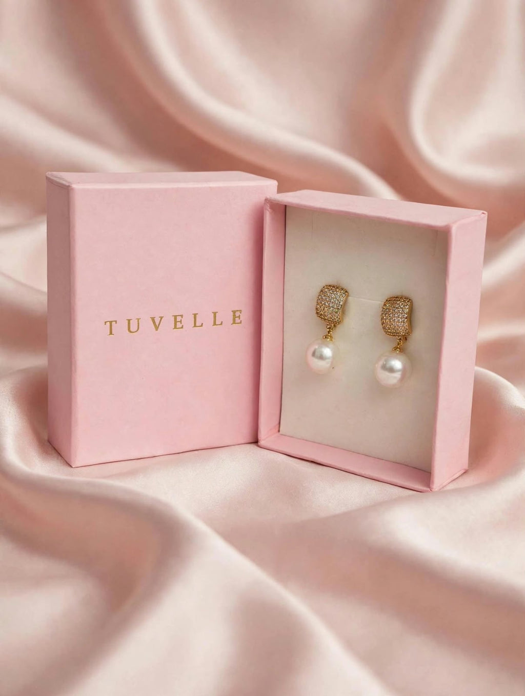 Top view of pearl-look drop earrings beside a pink TUVELLE box