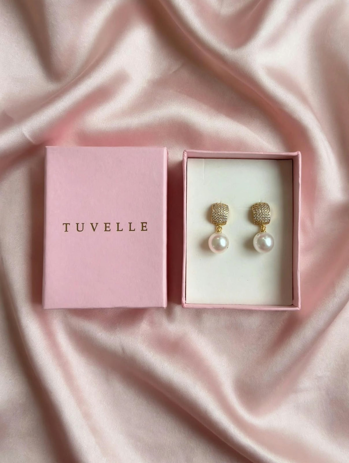 Angled view of gold-tone pearl-look drop earrings with pink TUVELLE packaging