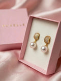 Close-up of gold-tone sparkling tops and white pearl-look drop earrings in a pink box