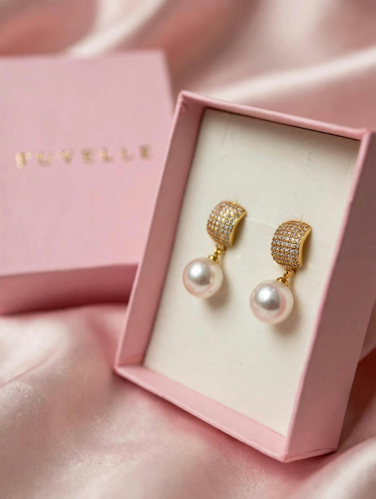 Close-up of gold-tone sparkling tops and white pearl-look drop earrings in a pink box