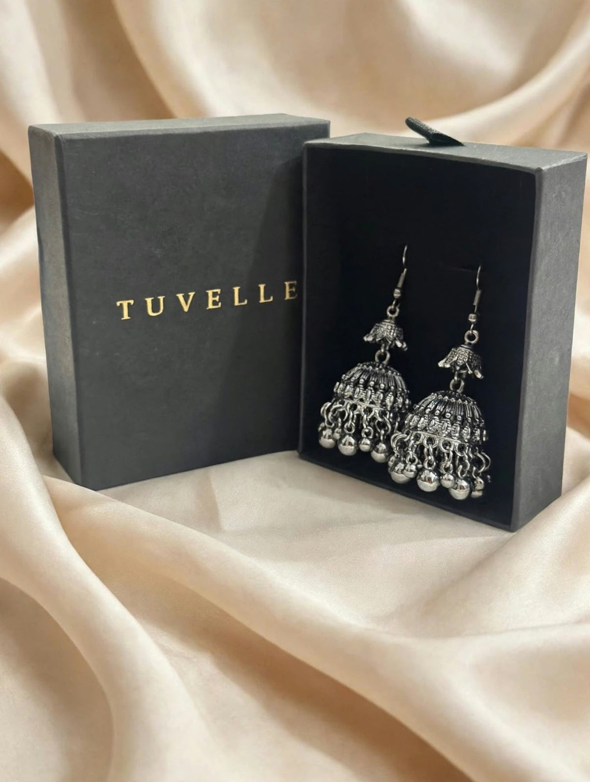 Silver-tone jhumka earrings displayed beside a black TUVELLE box
