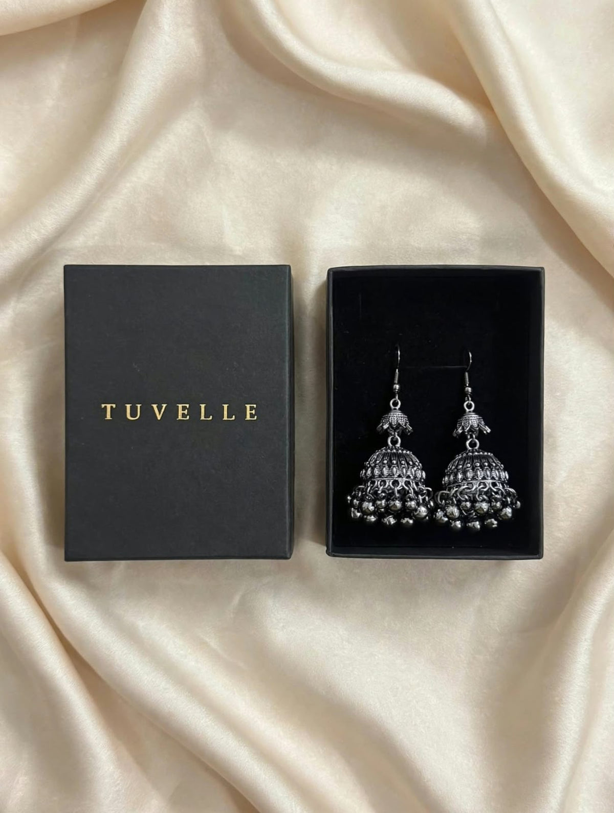 Close-up of antique silver-tone jhumka earrings with patterned domes and dangling bead fringe