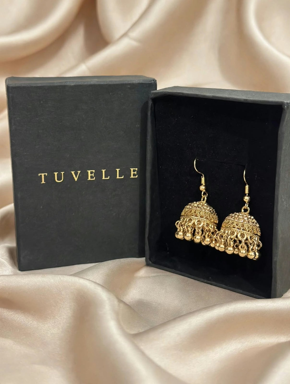 Top view of gold-tone jhumka earrings in black TUVELLE packaging on cream satin