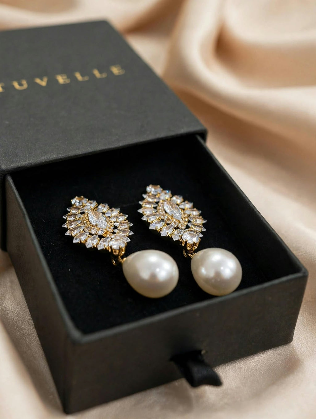 Angled view of sparkling floral pearl-look earrings in black packaging on cream satin